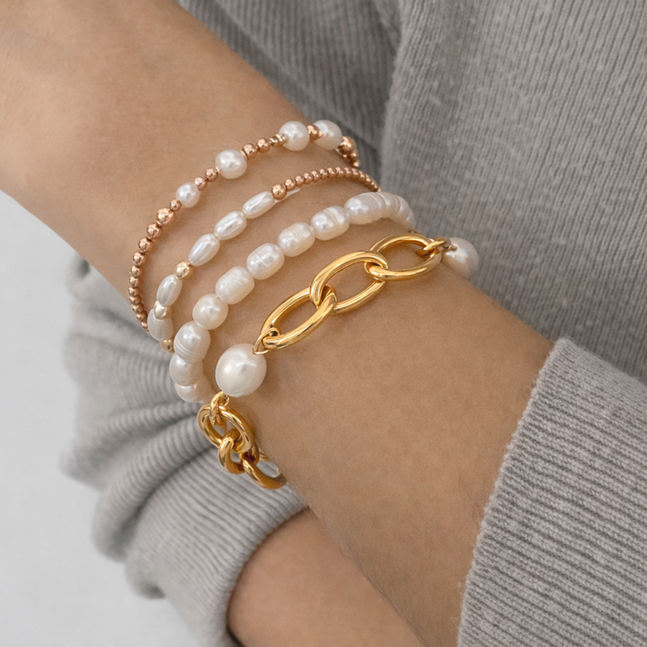 Stack of pearl and gold chain bracelets on a wrist against a neutral background